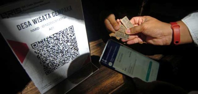 Petugas Bank Indonesia (BI) Tegal mempraktikkan cara melakukan pembayaran melalui aplikasi uang elektronik "server based", dompet elektronik dan mobile banking saat peluncuran dan implementasi QR Code Indonesian Standard (QRIS) untuk desa wisata di Pasar Slumpring, Desa Cempaka, Kabupaten Tegal, Jawa Tengah, Minggu (16/2/2019). - ANTARA FOTO/Oky Lukmansyah